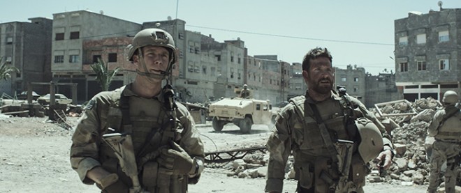 Photo Credit: Courtesy of Warner Bros. Pictures. Caption: (L-r) JAKE McDORMAN as Biggles and BRADLEY COOPER as Chris Kyle in Warner Bros. Pictures’ and Village Roadshow Pictures’ drama “AMERICAN SNIPER.”